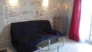 Un salon avec un mur en pierre, un canapé bleu foncé, une table basse en verre et un rideau rouge.