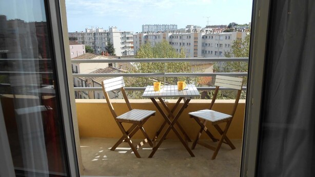 Un balcon avec une table et deux chaises, donnant sur un paysage urbain composé de différents bâtiments.