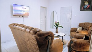 A living room with a brown leather sofa, a flat-screen TV mounted on the wall, a white door, and a framed picture on the wall.