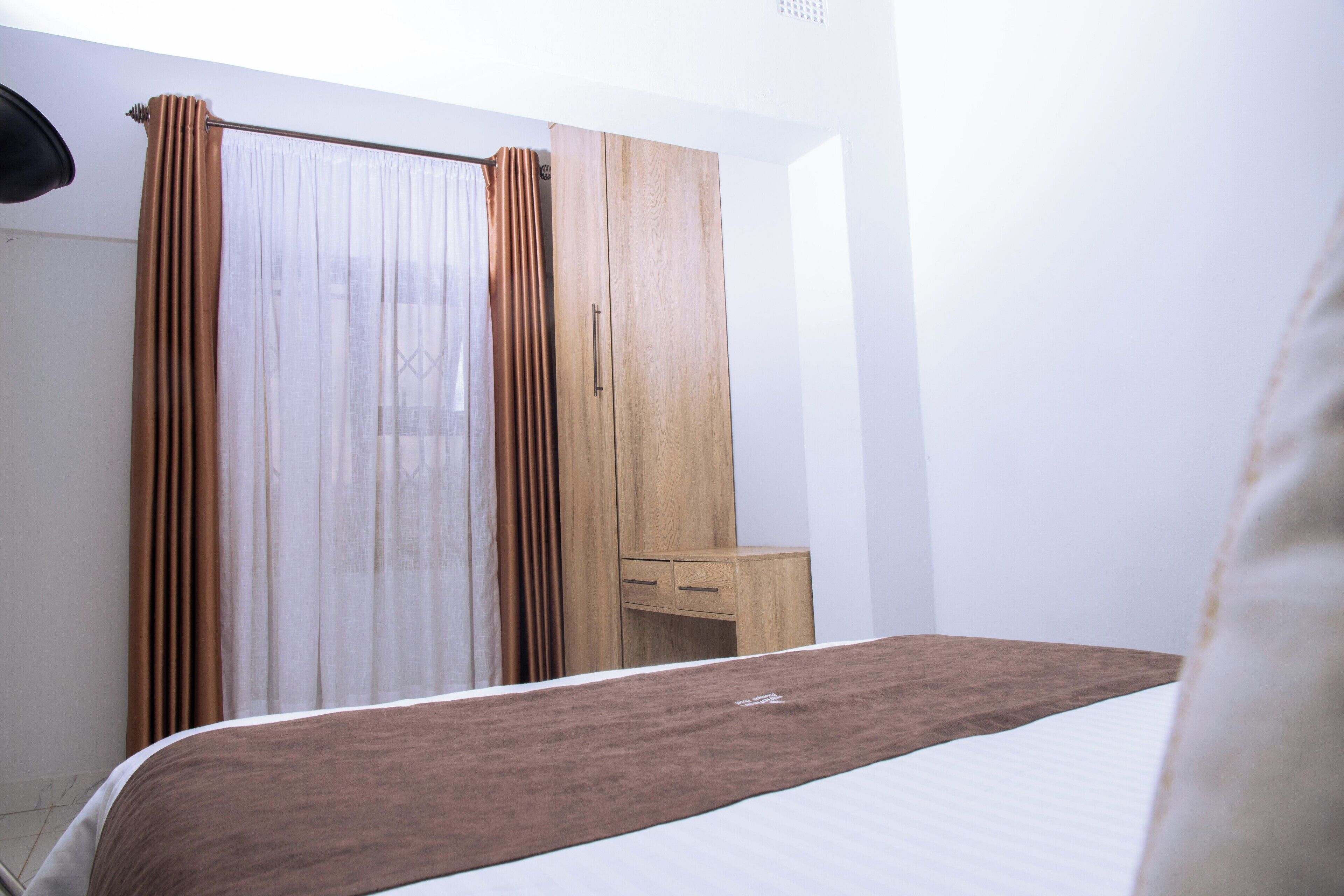 Un dormitorio con cama, armario de madera, mesita de noche y ventana con cortinas.