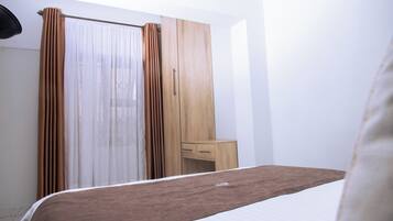 Un dormitorio con cama, armario de madera, mesita de noche y ventana con cortinas.
