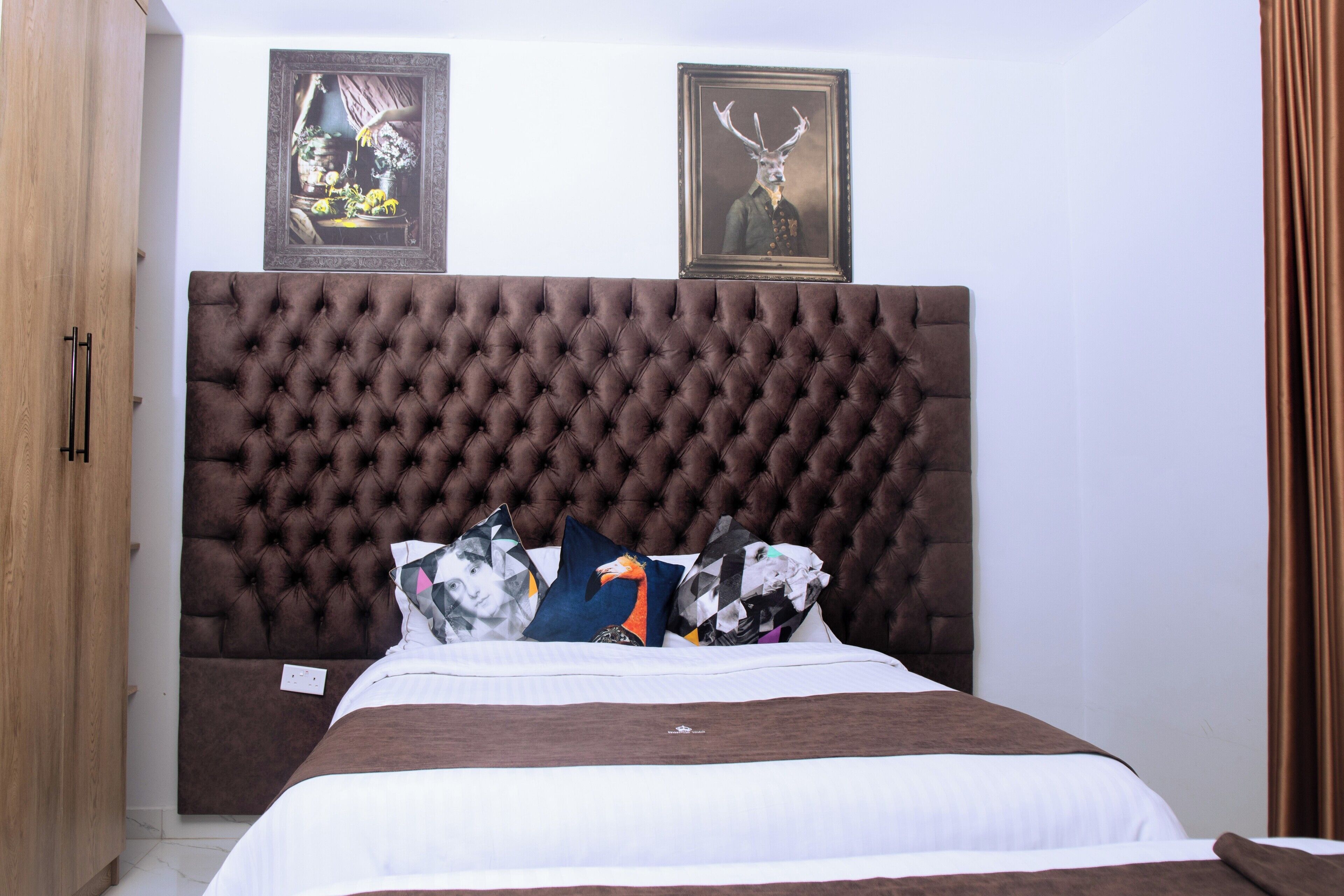 Un dormitorio con cabecera capitonada, cama con ropa de cama blanca y marrón, y dos cuadros en la pared.