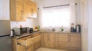 A kitchen with wooden cabinets, a microwave, a kettle, and a window with curtains.