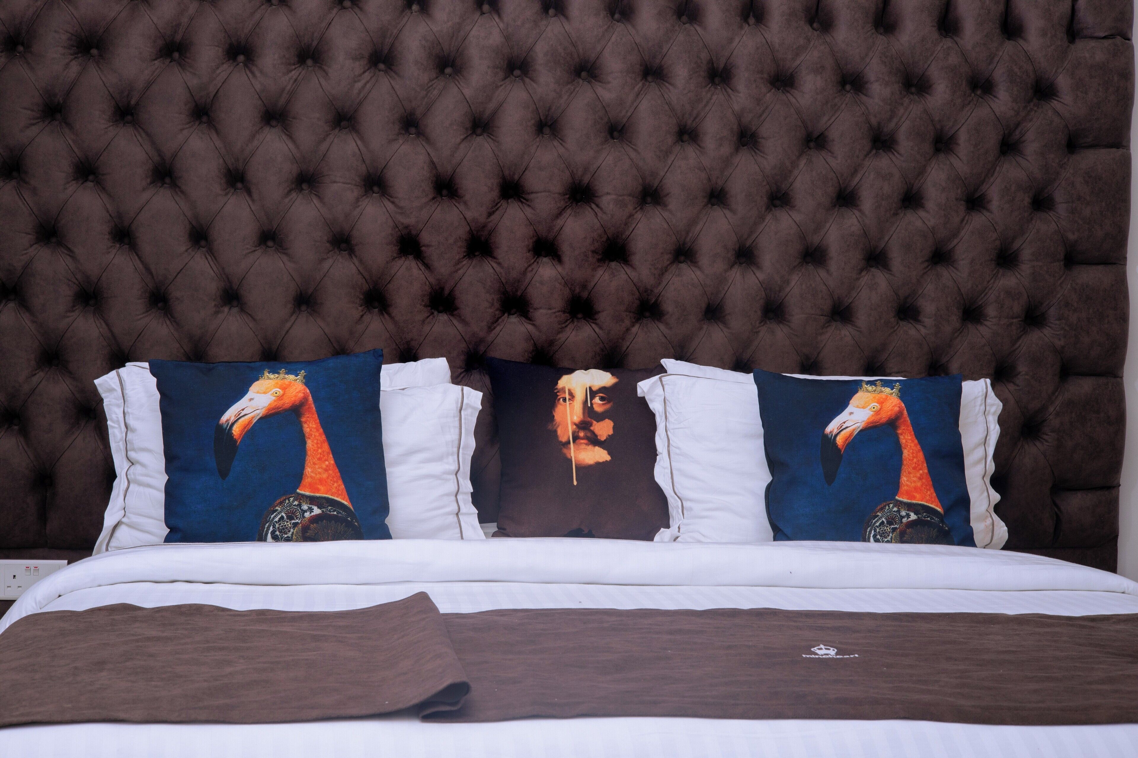 Una cama con cabecera capitonada, ropa de cama blanca y tres almohadas con diseños de pájaros.