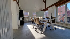 A spacious room with a high ceiling, a large window, and a white desk with chairs. - Project JUNE (Jueterbog)