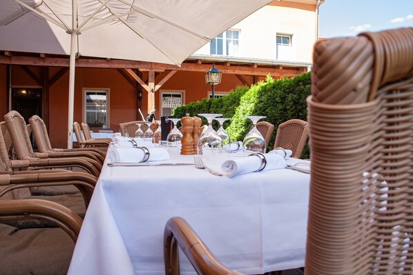 An outdoor dining area with wicker chairs and tables set up for a meal. - Project JUNE (Jueterbog)