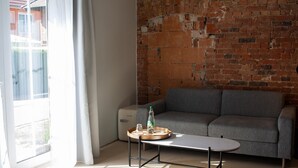 A living room with a grey sofa, a small round table, and a brick wall. - Project JUNE (Jueterbog)