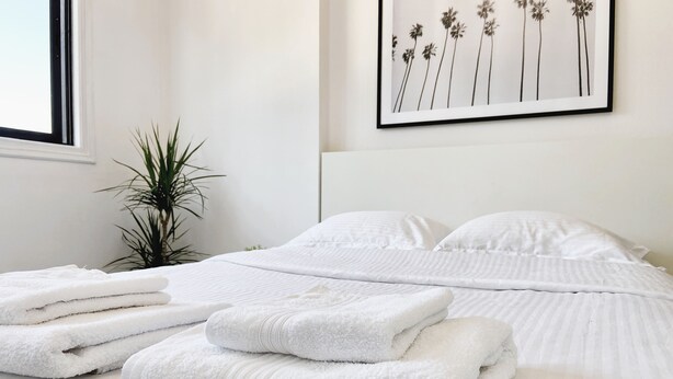 A neatly made bed with white linens and towels, a potted plant, and a framed picture on the wall. - ★ Modern studio in City Center, 5min from Beach ★ (Larnaca)