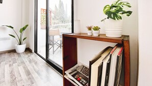 A modern interior with a wooden floor, a large window, and a bookshelf with books and plants. - ★ Modern studio in City Center, 5min from Beach ★ (Larnaca)