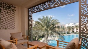 A balcony with wooden furniture, a pool, palm trees, and a view of other buildings. - Vesta - El Gouna Residence (El Gouna)