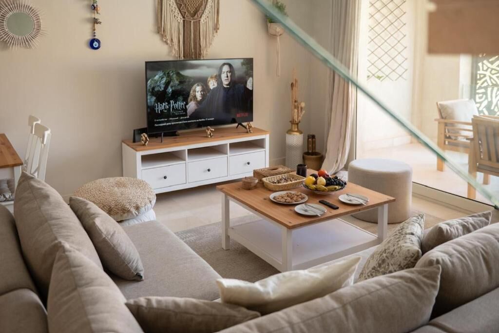 Una sala de estar con un sofá, una mesa de centro y un televisor mostrando un cartel de película.