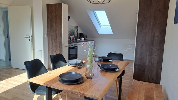 Ein Essbereich mit Holztisch, schwarzen Stühlen und einer Blumenvase.
