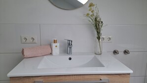 Ein Badezimmer mit einem weißen Waschbecken, einem Spiegel, einer Vase mit Blumen, einem Handtuch und einer Flasche Savage Garden Körperwäsche.