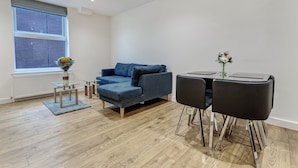 A modern living room with a blue sofa, a glass coffee table, and a dining table with chairs. - 1 Bed, Sleeps 3, Free Parking, Wifi (Slough)