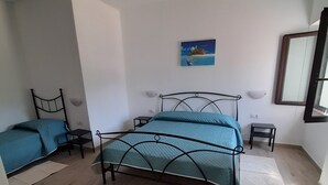 A bedroom with a bed, a chair, a small table, a nightstand, a painting, and a mirror.