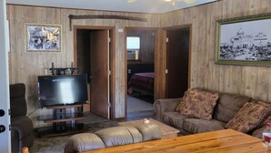 A living room with a television, a sofa, a coffee table, and a door leading to a bedroom.
