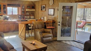 A cozy cabin interior with a wooden dining area, a leather chair, a sofa, and a view of a deck through a glass door.