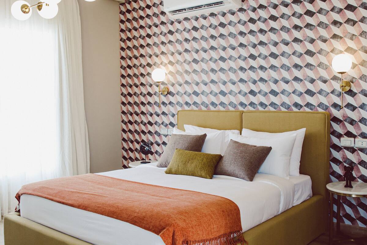 A modern hotel room with a large bed, a patterned wall, and a ceiling fan.