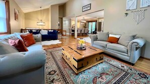 A spacious living room with a high ceiling, a ceiling fan, and a dining area visible through an open doorway. - HillTop Manor-Spacious 6BR+PS5+FirePit+Pool Table (Lake,Ariel)