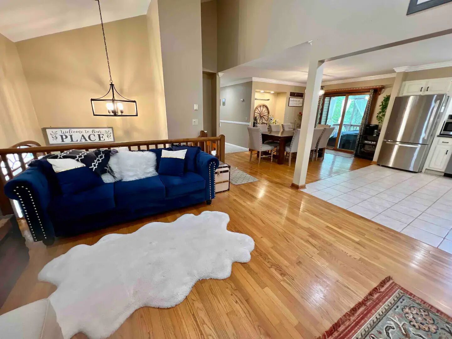 A spacious living area with a blue sofa, a white shag rug, and a dining area with a chandelier.
