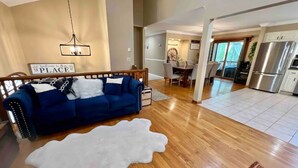 A spacious living area with a blue sofa, a white shag rug, and a dining area with a chandelier. - HillTop Manor-Spacious 6BR+PS5+FirePit+Pool Table (Lake,Ariel)