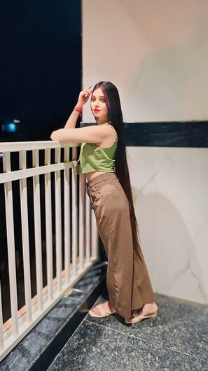 A person standing on a balcony with a railing, wearing a green top and brown pants. - Raksha Suites & Banquet Greater Noida (Greater Noida)