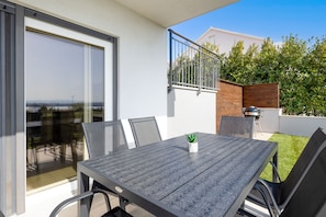 A modern outdoor dining area with a table and chairs, a small potted plant, and a view of the city through a glass door. - Stunning 2-bed Apartment in Kastela (Kastela)