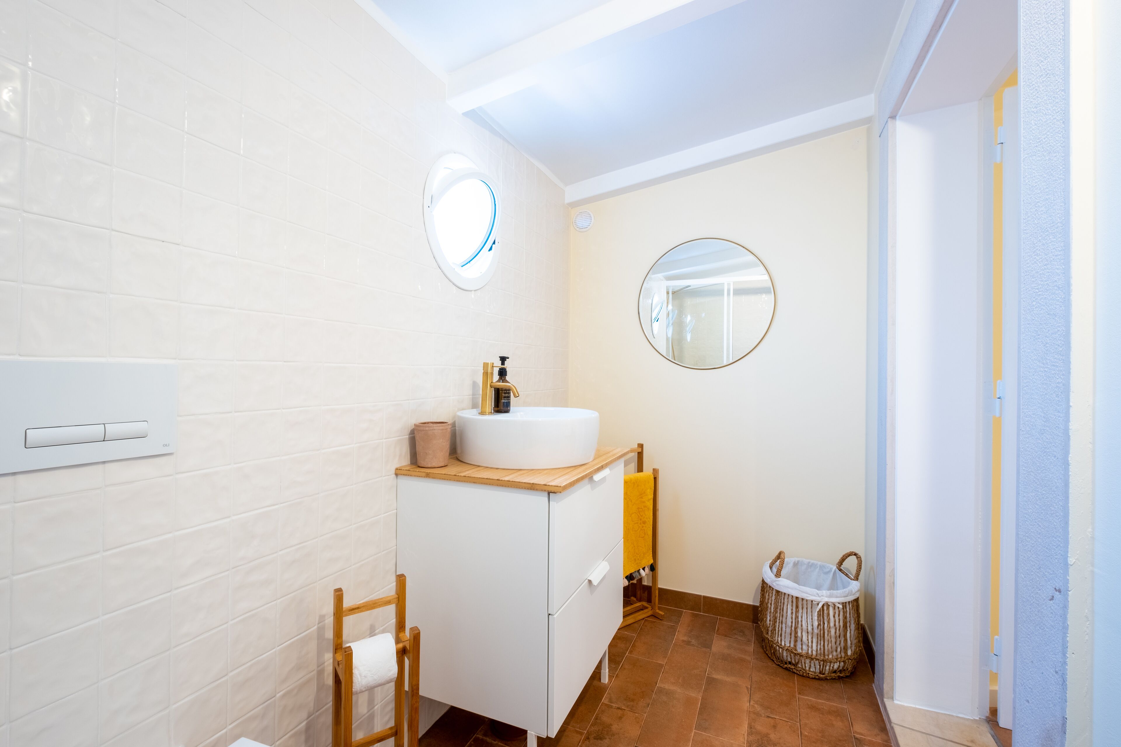 A modern bathroom with a white sink, wooden cabinet, two round mirrors, a towel rack, and a wicker basket.