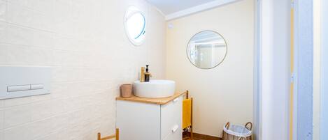 A modern bathroom with a white sink, wooden cabinet, two round mirrors, a towel rack, and a wicker basket.