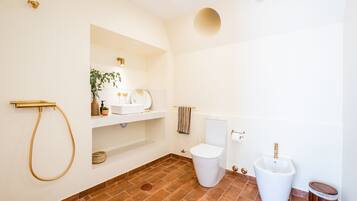 A modern bathroom with a white toilet, bidet, and a gold shower hose.