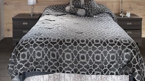 A bedroom with a sloped ceiling, two windows, a bed with patterned bedding, two bedside tables with lamps, and a nightstand with a lamp. - Charming chalet with WiFi in Saint-Donat (Saint-Donat)