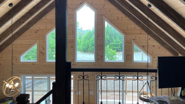 A spacious room with a high ceiling, wooden beams, and large windows offering views of a forested area. - Charming chalet with WiFi in Saint-Donat (Saint-Donat)