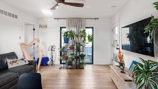 A spacious living room with a wooden floor, a black sofa, a harp, and a plant shelf. - Pet-Friendly Carriage House Close to Downtown (Indianapolis)