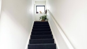 A staircase with black steps leading to a landing area with a window and a plant. - Pet-Friendly Carriage House Close to Downtown (Indianapolis)