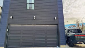 A dark-colored garage door with a small window above it and two exterior wall-mounted lights. - Pet-Friendly Carriage House Close to Downtown (Indianapolis)