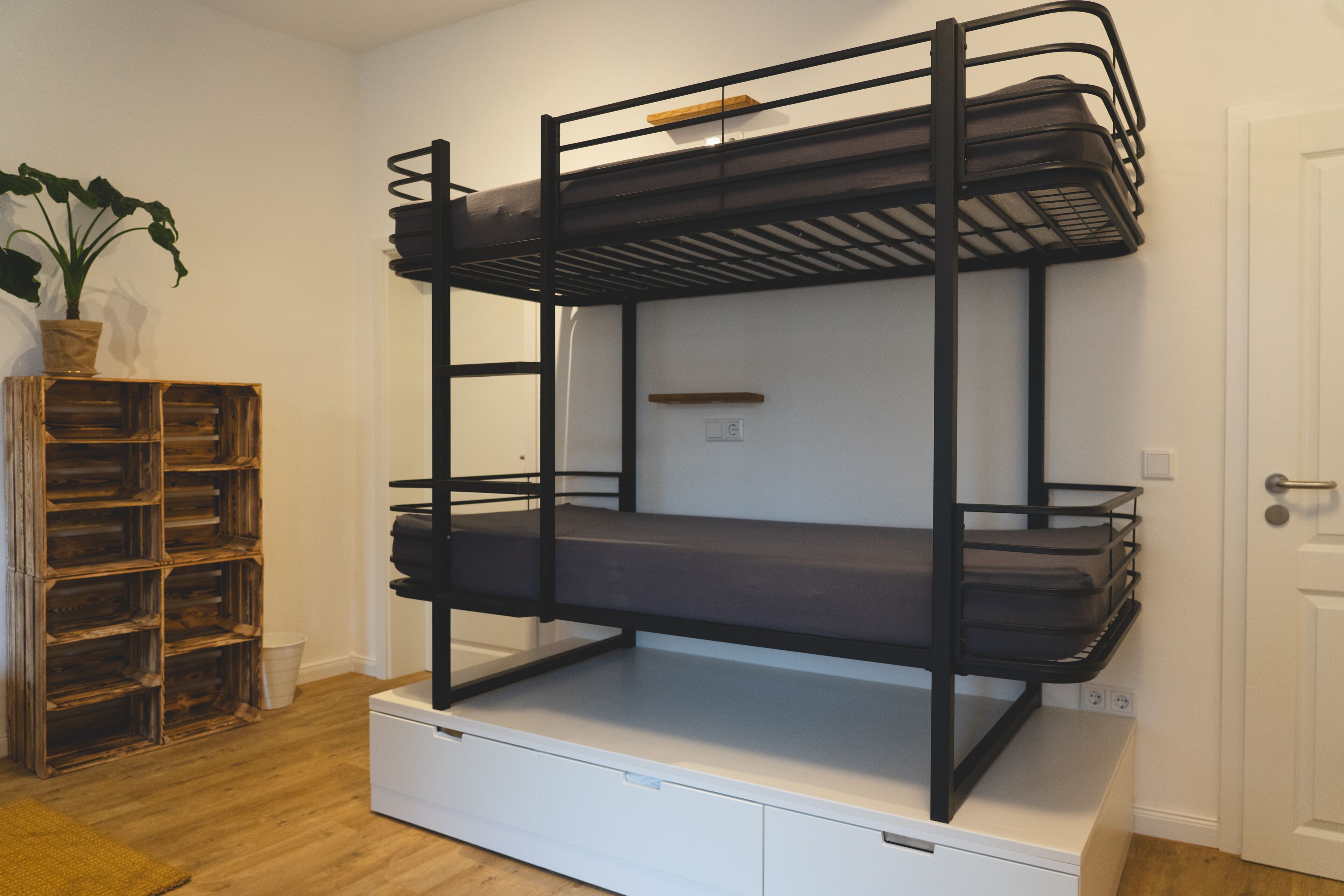 A bunk bed with a storage drawer underneath, a wooden crate, and a potted plant.