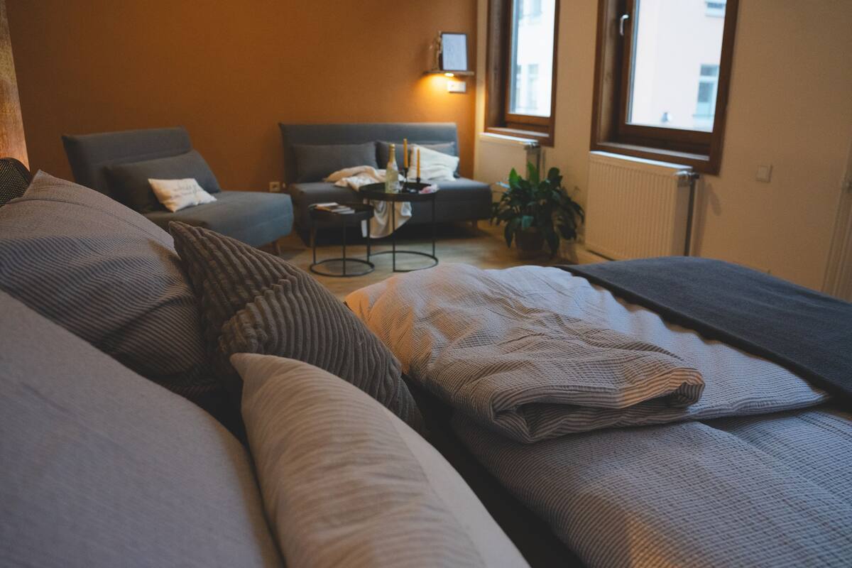 A cozy hotel room with a bed, a sofa, a small table with candles, and a potted plant.
