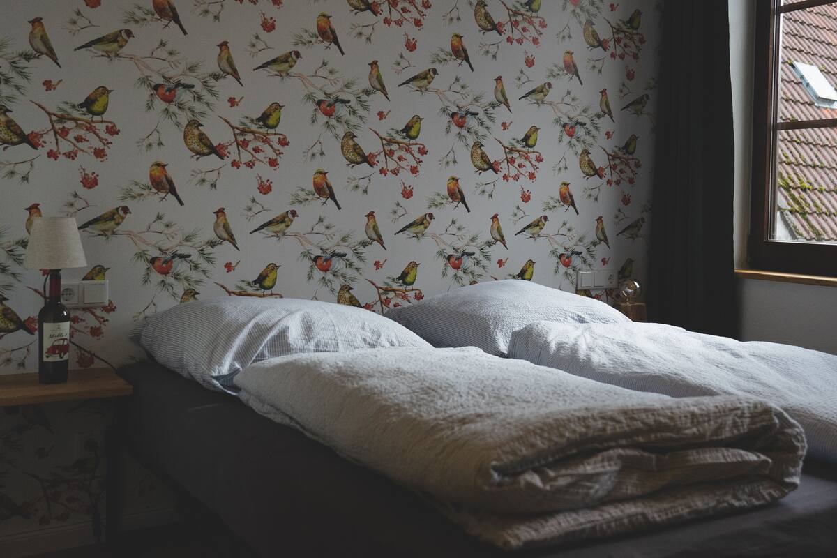 A bedroom with a bed, pillows, a lamp, and a bottle on a nightstand.