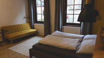 A room with a sofa, a bed with two pillows, a floor lamp, and a view through a window.