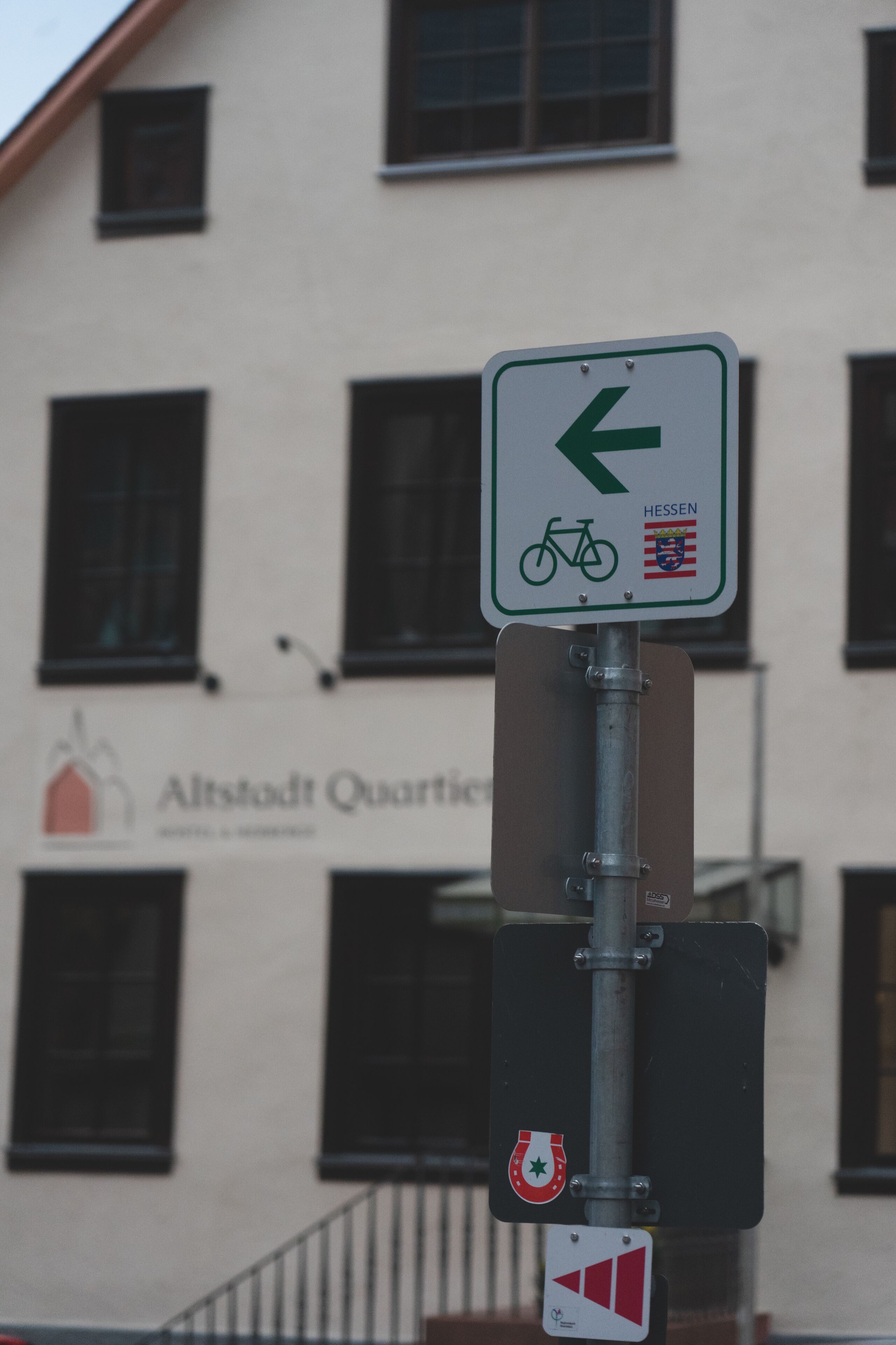 Una señal direccional con un símbolo de bicicleta y la palabra 'HESSEN' en la fachada de un edificio.