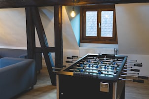 Quarto com mesa de futebol, sofá e janela com radiador.