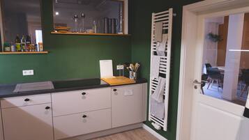 A kitchen with a black countertop, white cabinets, a wooden cutting board, and a hanging rack with towels.