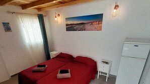 A room with two beds, a small table, a refrigerator, and a window with curtains.