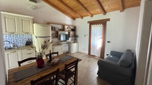 Uma cozinha compacta com armários de madeira, uma mesa de jantar com cadeiras, um sofá e uma televisão.