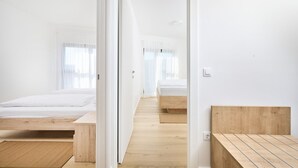 A modern hotel room with a wooden floor, white walls, and a large bed. - Ferienwohnung Tamar - 6 Personen, 2 Schlafzimmer, Balkon (Umag)