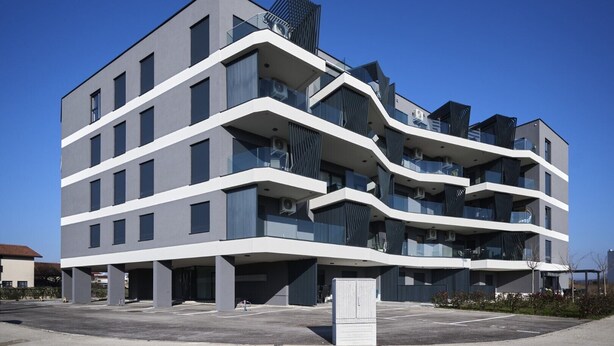 A modern multi-story building with a unique wavy facade, balconies with dark railings, and a parking area in front. - Ferienwohnung Tamar - 6 Personen, 2 Schlafzimmer, Balkon (Umag)