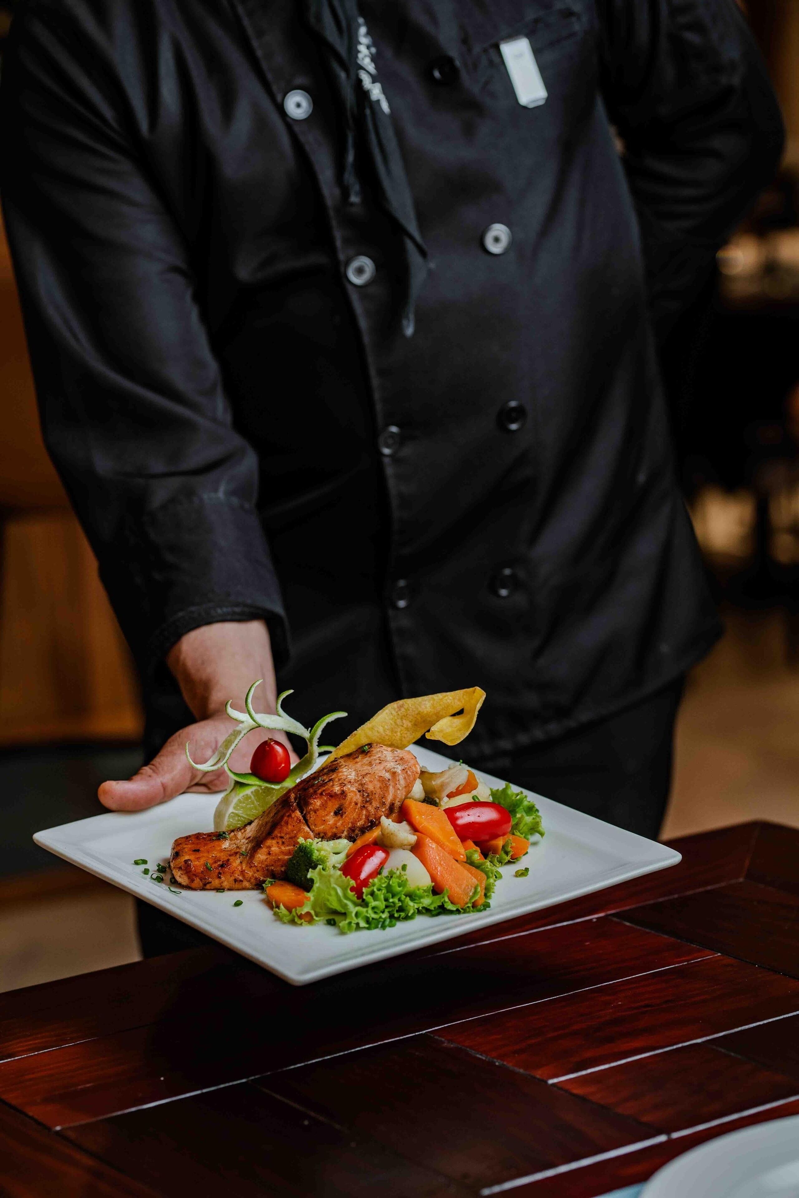 Uno chef che tiene un piatto con pollo alla griglia e verdure.