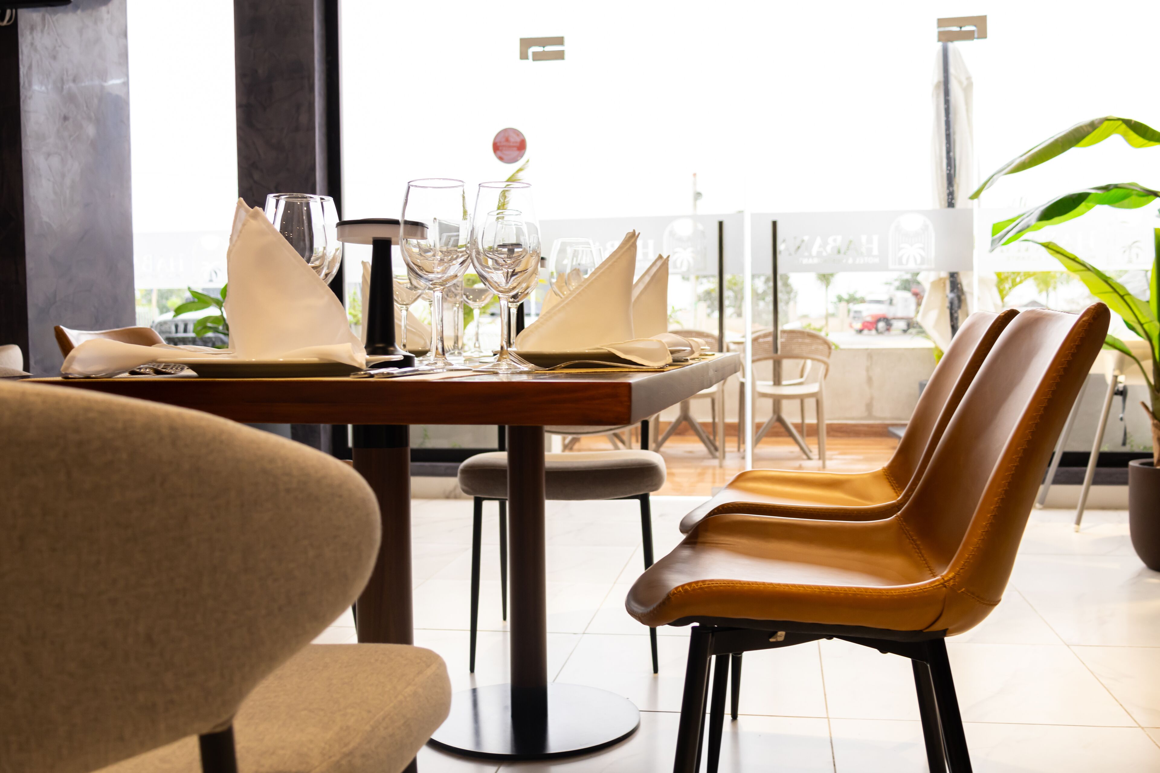 A restaurant with a table set for two, chairs, and a view of the outside.