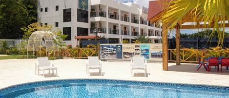 A hotel with a swimming pool, lounge chairs, and a palm tree.