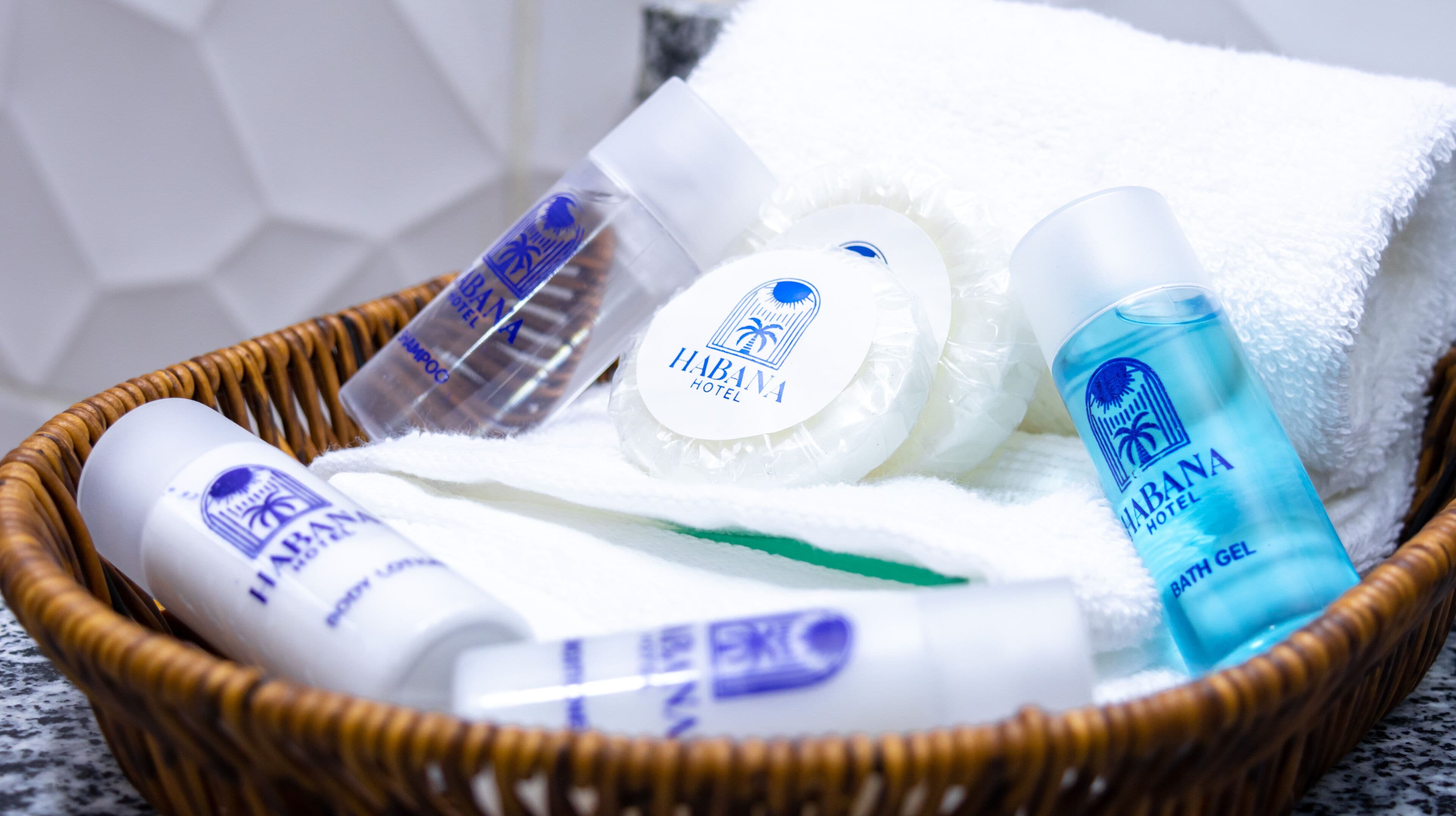A wicker basket containing toiletries including a bottle of shampoo, a bar of soap, a towel, and a bottle of bath gel.